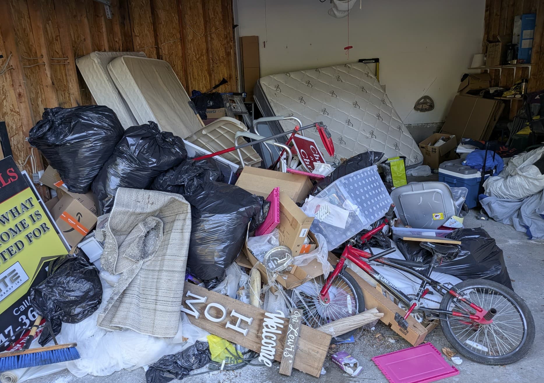 A garage full of junk for removal — mattresses, bagged trash, boxes, and an old bike
